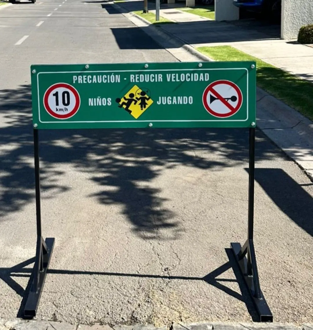 Barrera metálica con letrero verde «Precaución, reducir velocidad», 10 km/h, niños jugando y prohibido tocar bocina