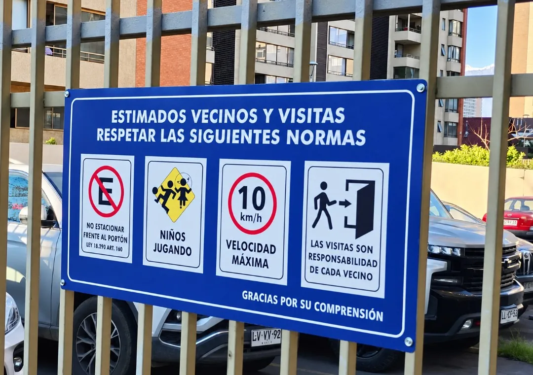 Letrero azul con normas para vecinos y visitas, instalado en una reja